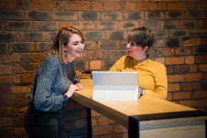 Two women working and laughing in bare brick office